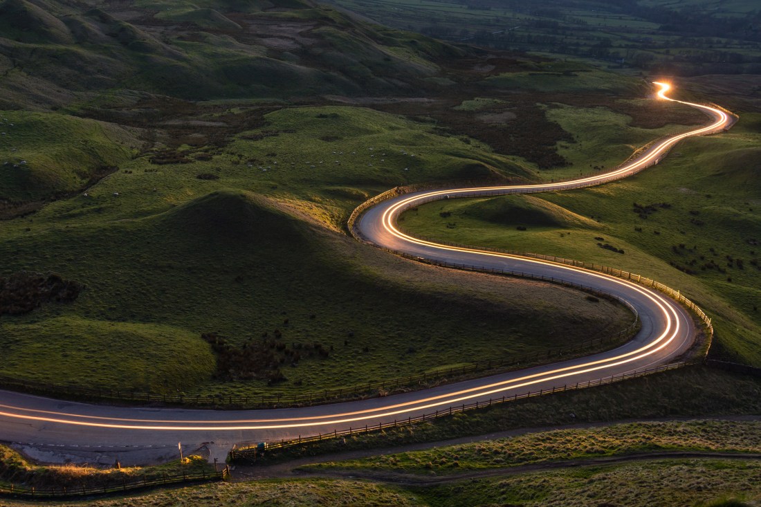 Winding curvy rural road with light trail from headlights leading through British countryside.