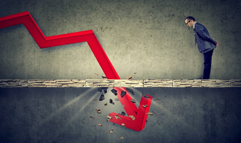 Depressed business man looking down at the falling red arrow going through a concrete floor. Fall and depreciation concept.