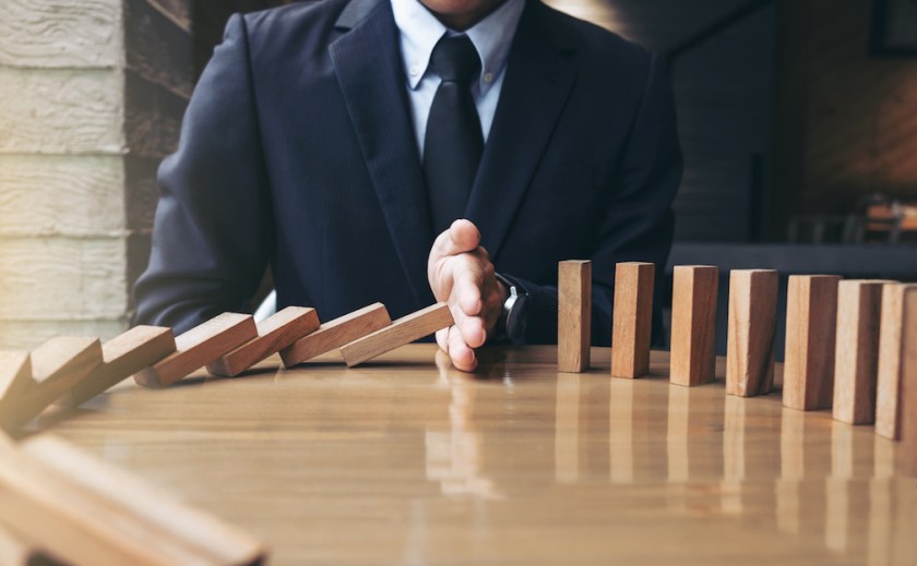 Close up of businessman hand Stopping Falling wooden Dominoes effect from continuous toppled or risk, strategy and successful intervention concept for business
