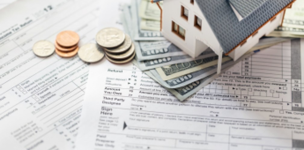 Miniature house with money on tax papers