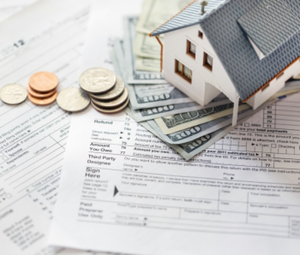 Miniature house with money on tax papers