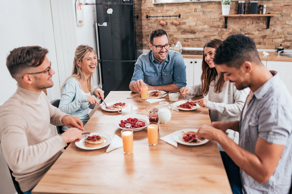 Friends sitting around wooden table, eating dessert and having fun.
