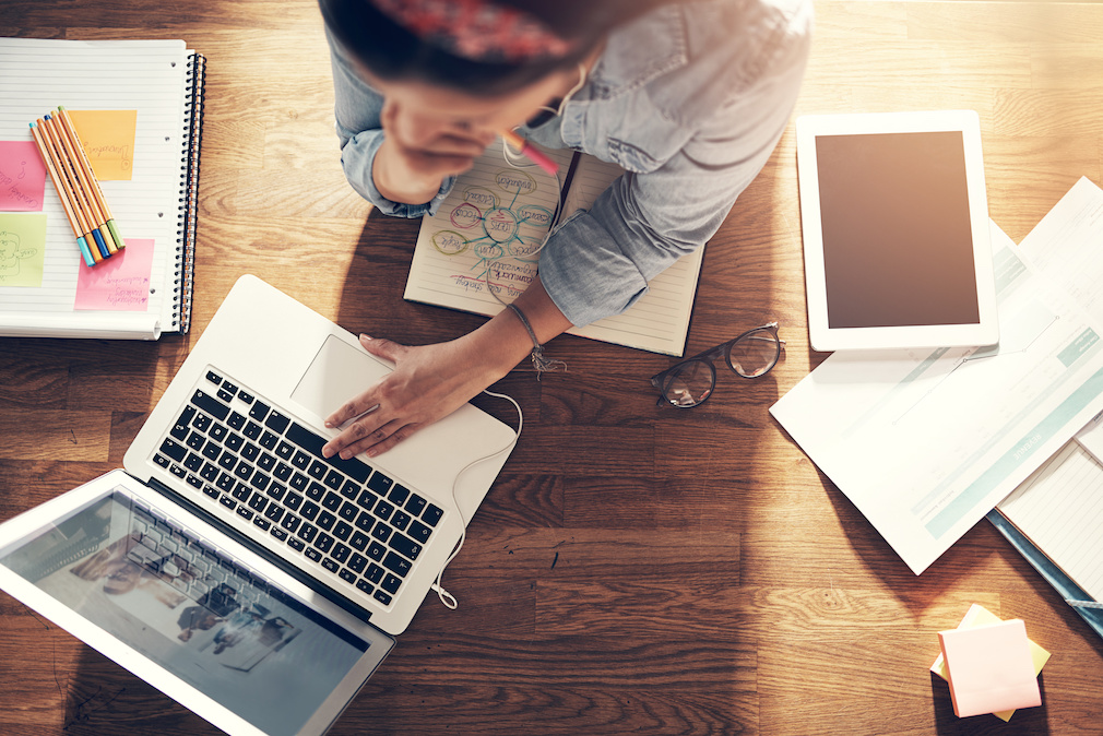 Young female entrepreneur thinking and browsing laptop in office