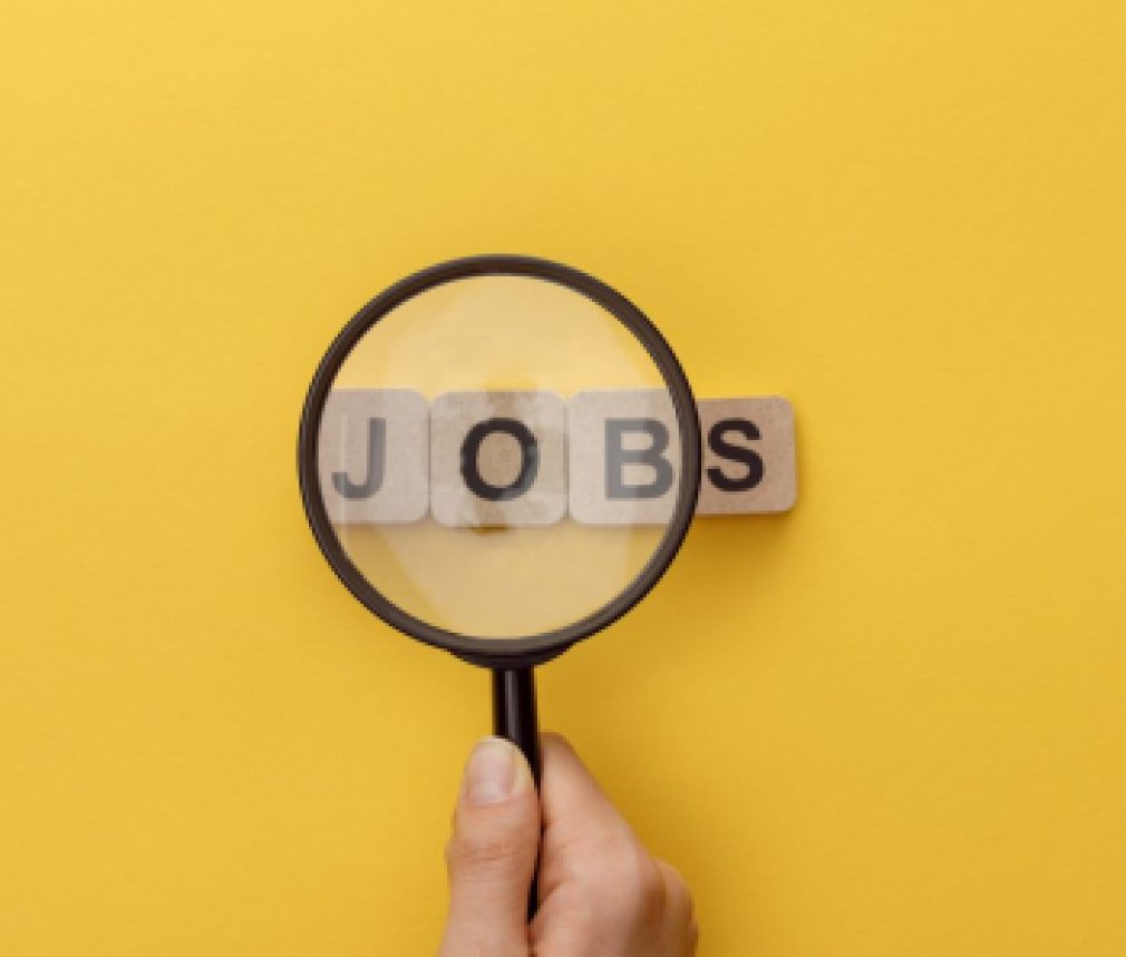 cropped view of woman holding magnifying glass under cardboard squares with jobs lettering on yellow background