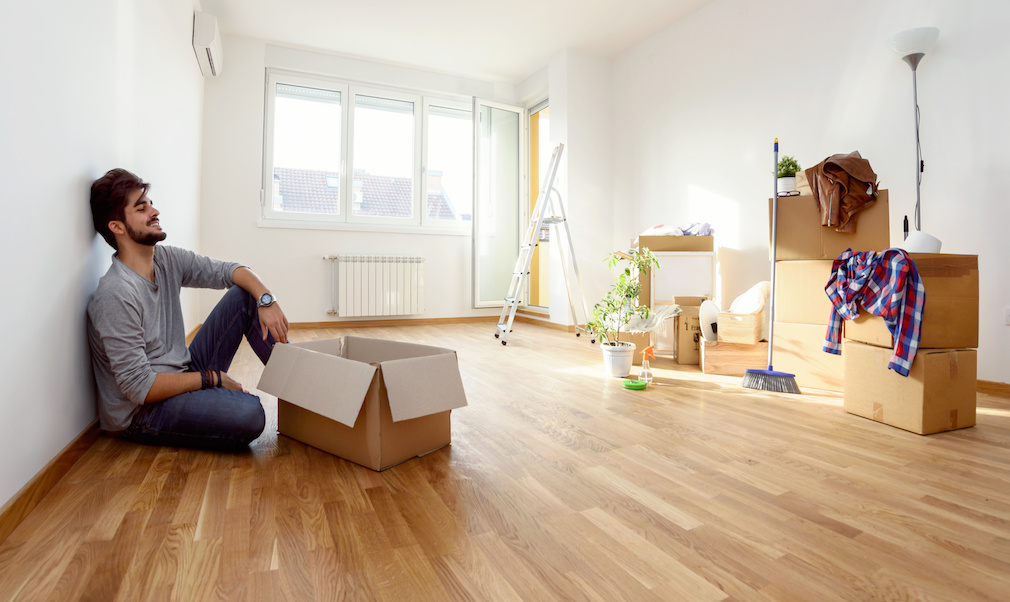 Happy young man just moved into new home unpacking boxes sitting on the floor