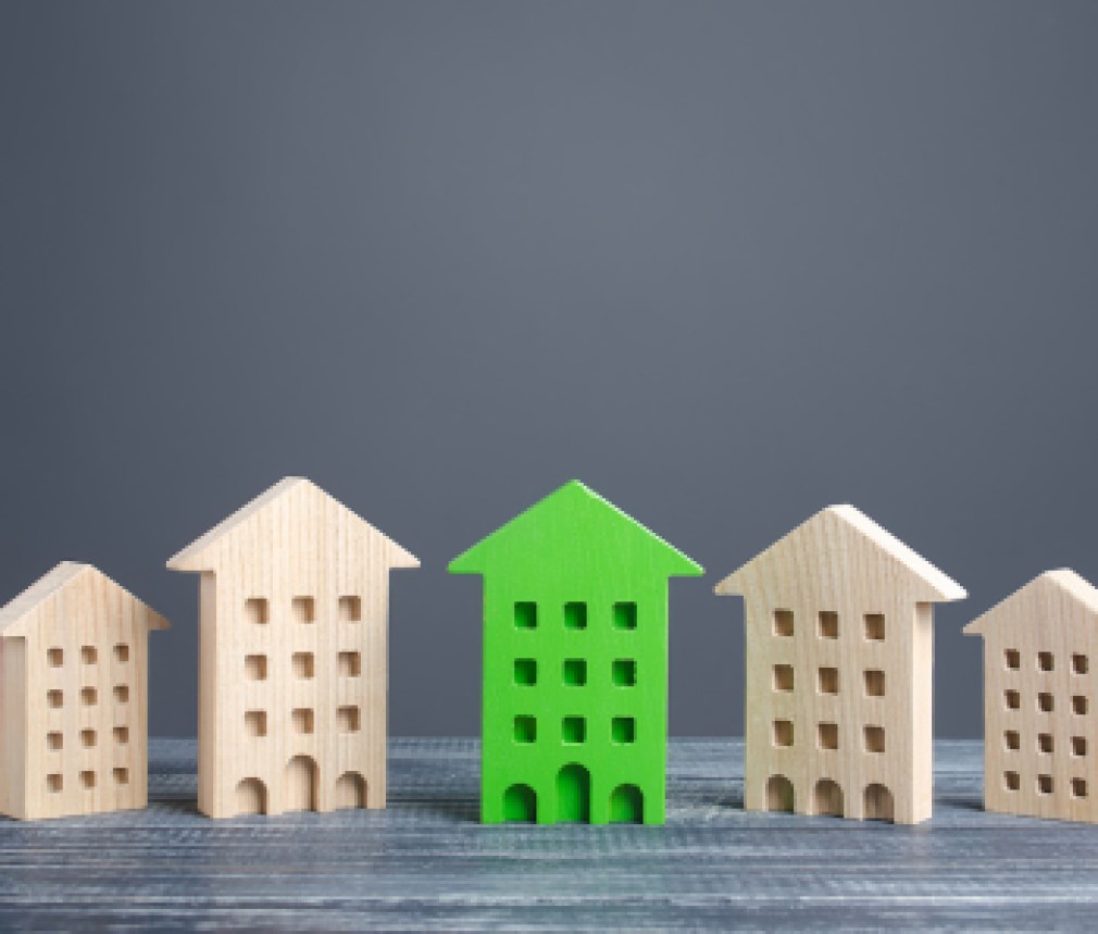 Green figure of a residential building stands out among rest of houses. Zero carbon emissions conservation energy saving technologies. Search best option apartment. High quality, convenient location.