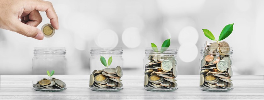 Hand putting coin in glass bottles with plants glowing, Saving money and investment concepts