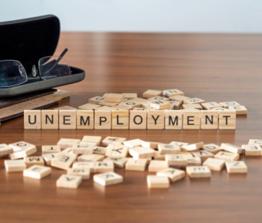 unemployment concept represented by wooden letter tiles on a wooden table with glasses and a book