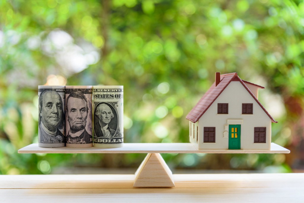 Home loan / reverse mortgage or transforming assets into cash concept : House model, US dollar notes on a simple balance scale, depicts a homeowner or a borrower turns properties / residence into cash