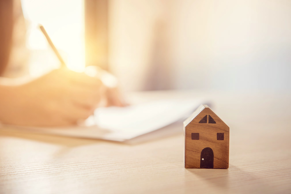 Close up wooden toy house with Woman signs a purchase contract or mortgage for a home, Real estate concept.