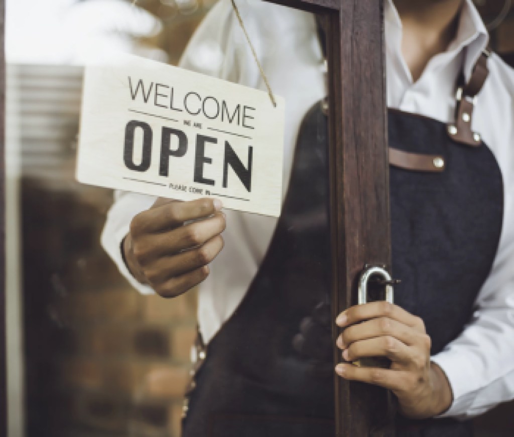 Store owner turning open sign broad through the door glass and ready to service.