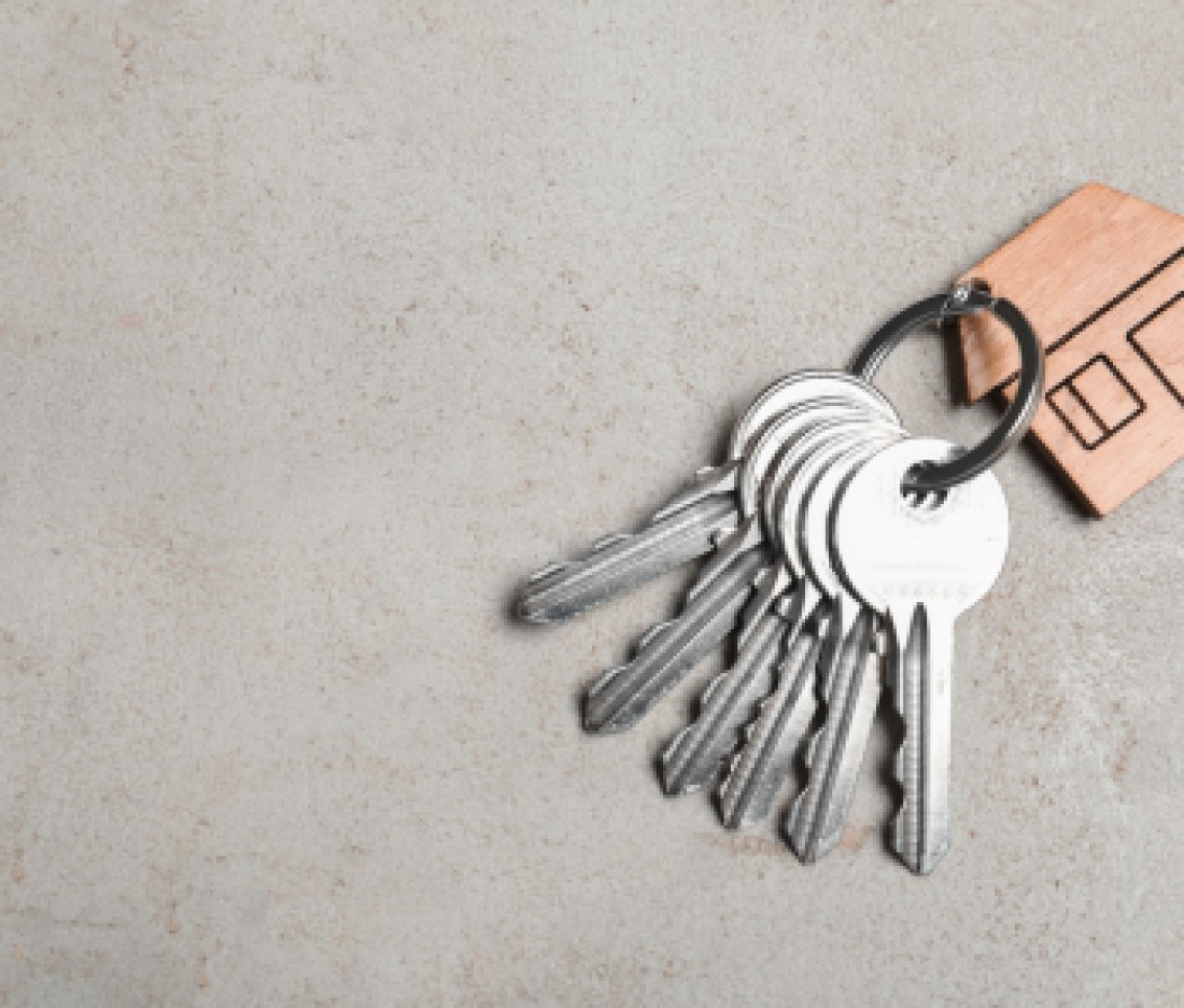 Keys with trinket in shape of house on grey stone background, top view and space for text. Real estate agent services