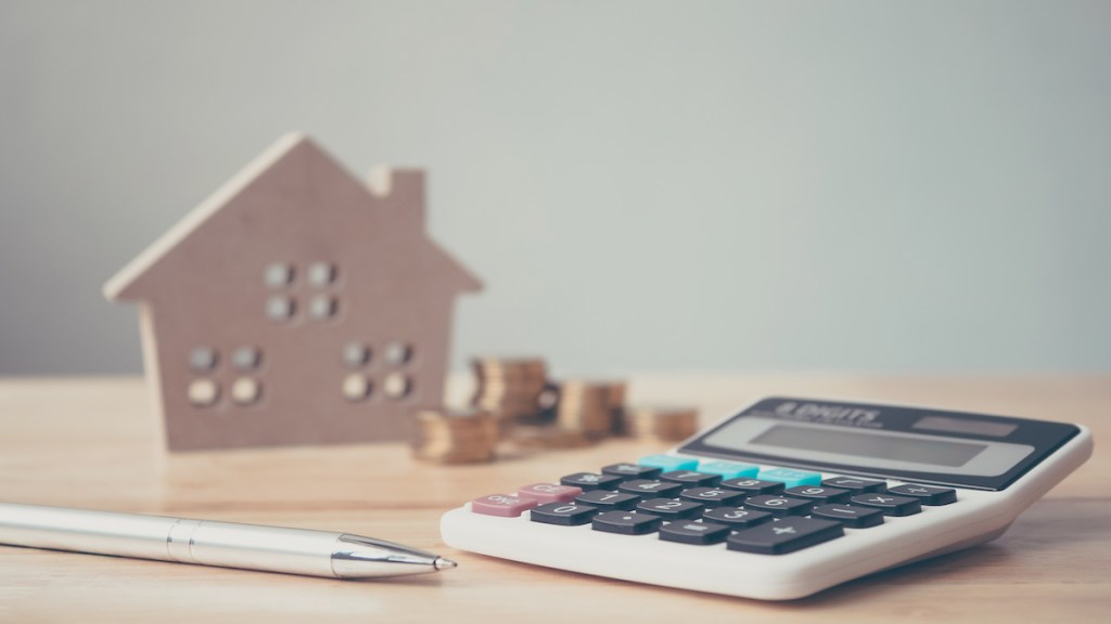 Calculator with wooden house and coins stack and pen on wood table. Property investment and house mortgage financial concept