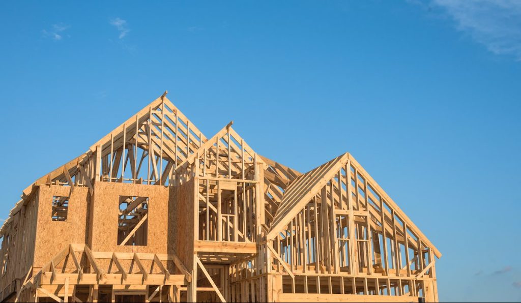 Close-up of gables roof on stick built home under construction and blue sky in Humble, Texas, USA. New build roof with wooden truss, post and beam framework. Timber frame house, real estate background