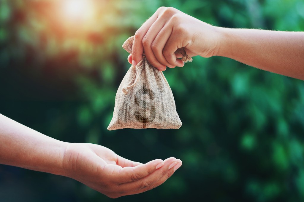 hand giving money bag to another people on green background with sunrise