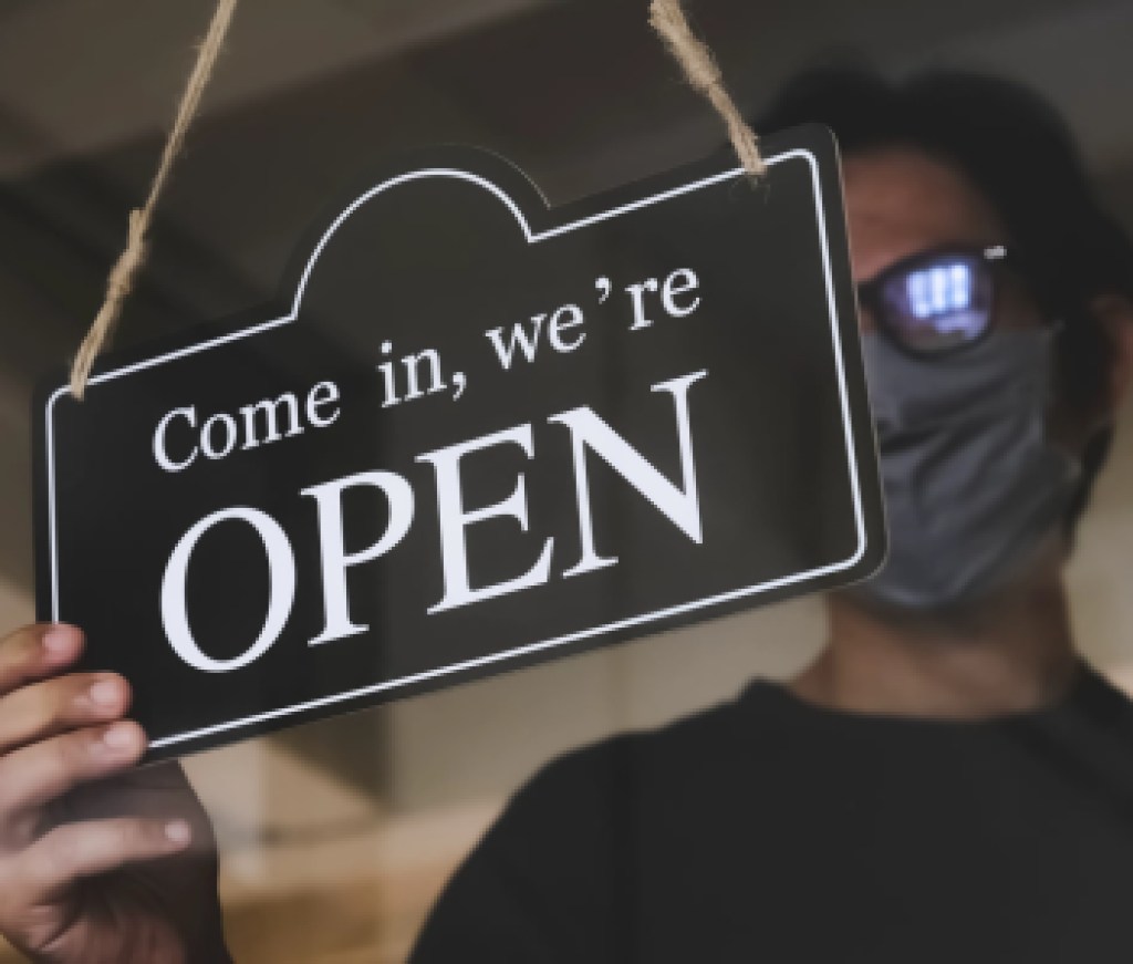 the state allows retail stores or restaurants and businesses to reopen after coronavirus restrictions. man with face mask turning a sign on a door shop. economy starts running after being on lockdown.