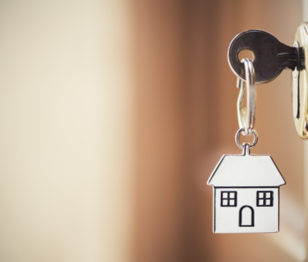 House key on a house shaped silver keyring in the lock of a door