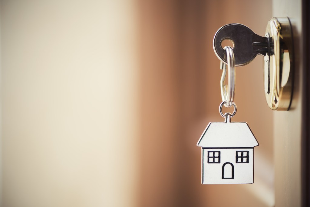 House key on a house shaped silver keyring in the lock of a door