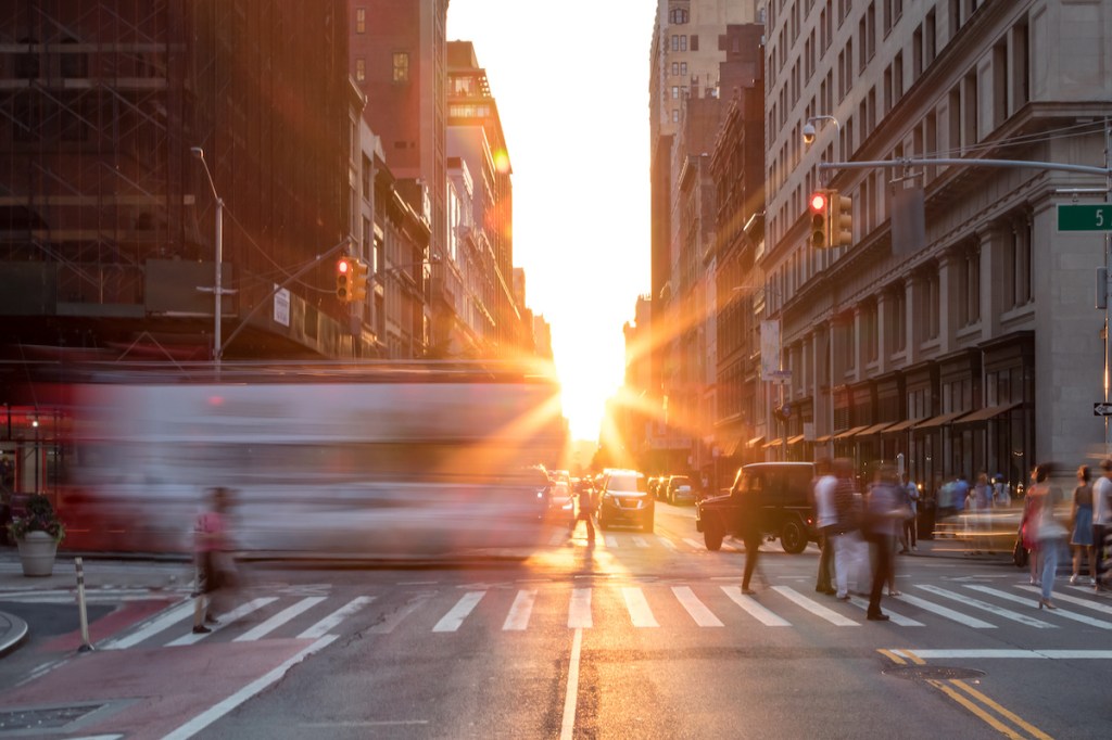 Busy New York City street scene with crowds of people in Midtown Manhattan with sunset background