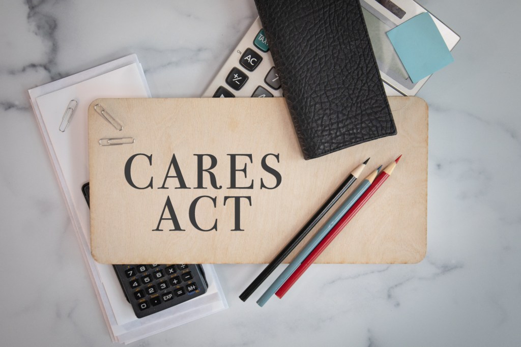 Cares Act sign on wooden sign with office materials laying around government financial aid programs small business relief