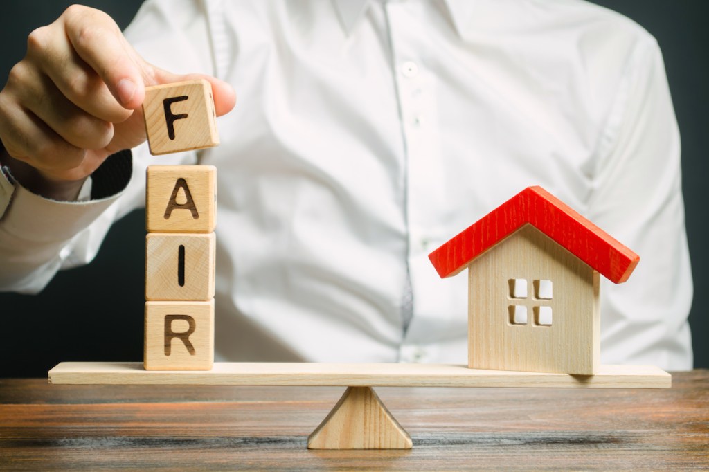 Wooden blocks with the word Fair and a wooden house. Fair value of real estate and housing. Property valuation. Home appraisal. Housing evaluator. Legal transparent deal. Apartment purchase / sale.