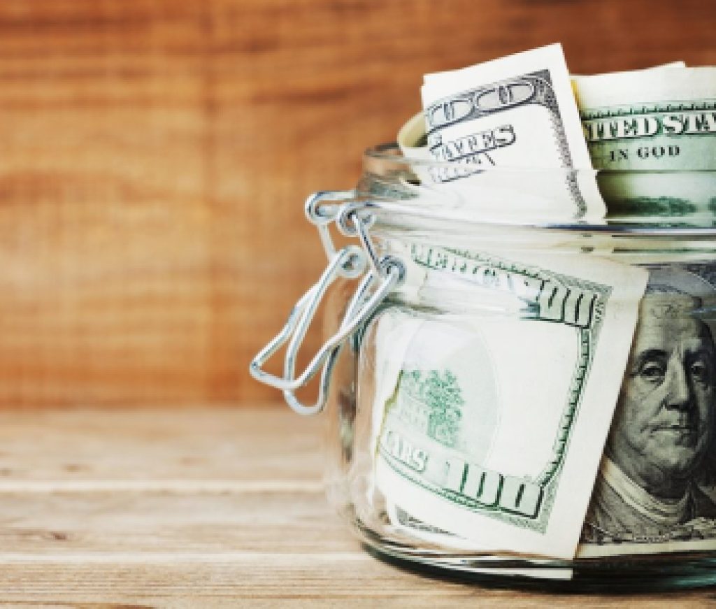 Dollar bills in glass jar on wooden background. Saving money concept.