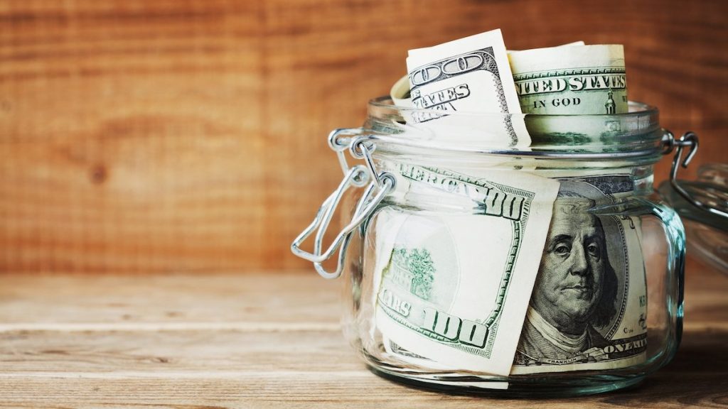 Dollar bills in glass jar on wooden background. Saving money concept.