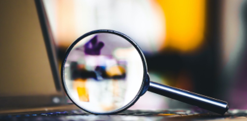 Magnifying glass on laptop keyboard. Internet security concept background.