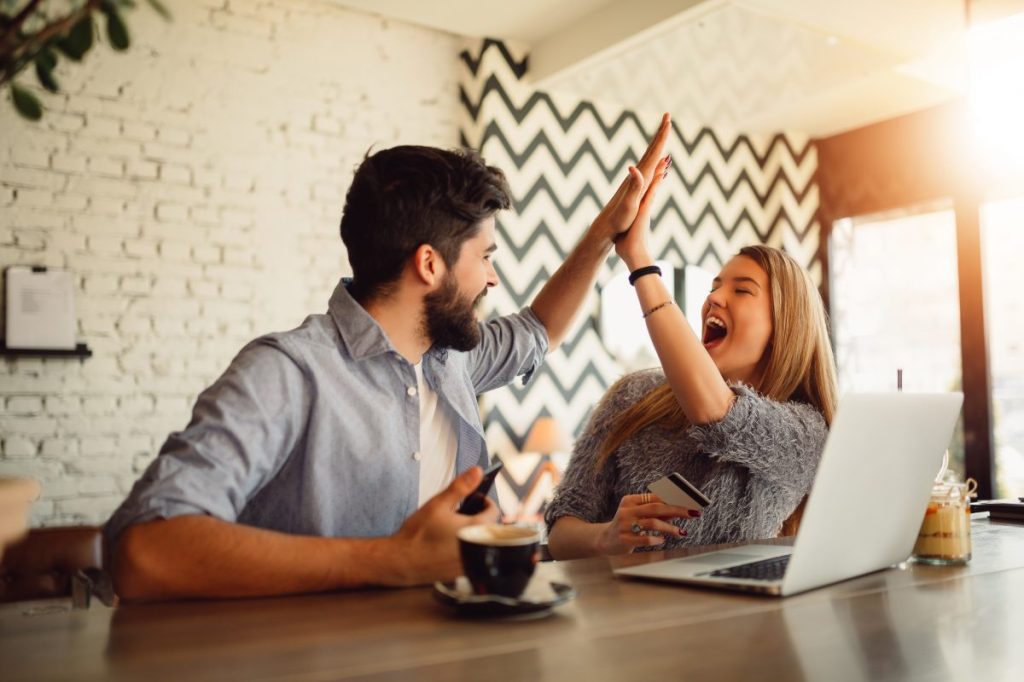 Portrait of an excited young couple giving high five while shopping online.