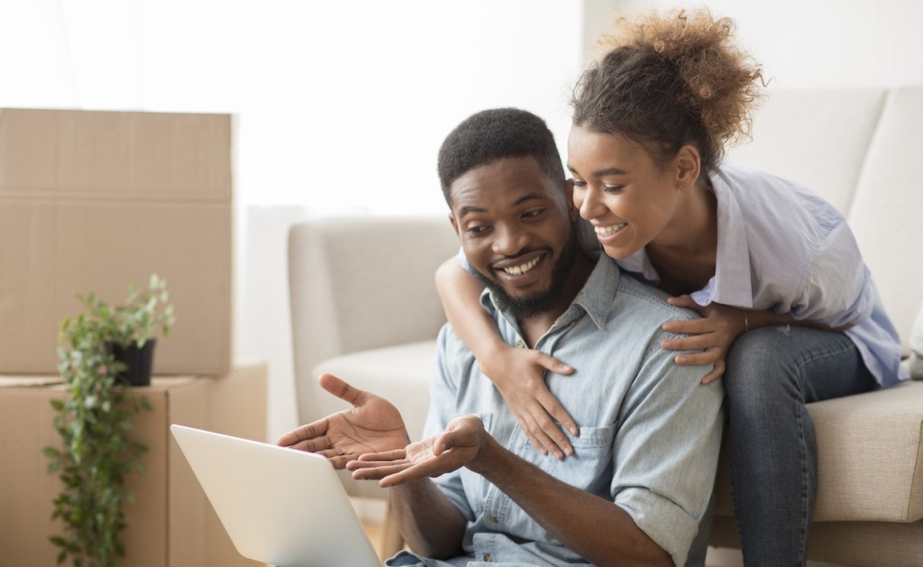 Husband Using Laptop Showing Something Wife Sitting On Couch Indoor