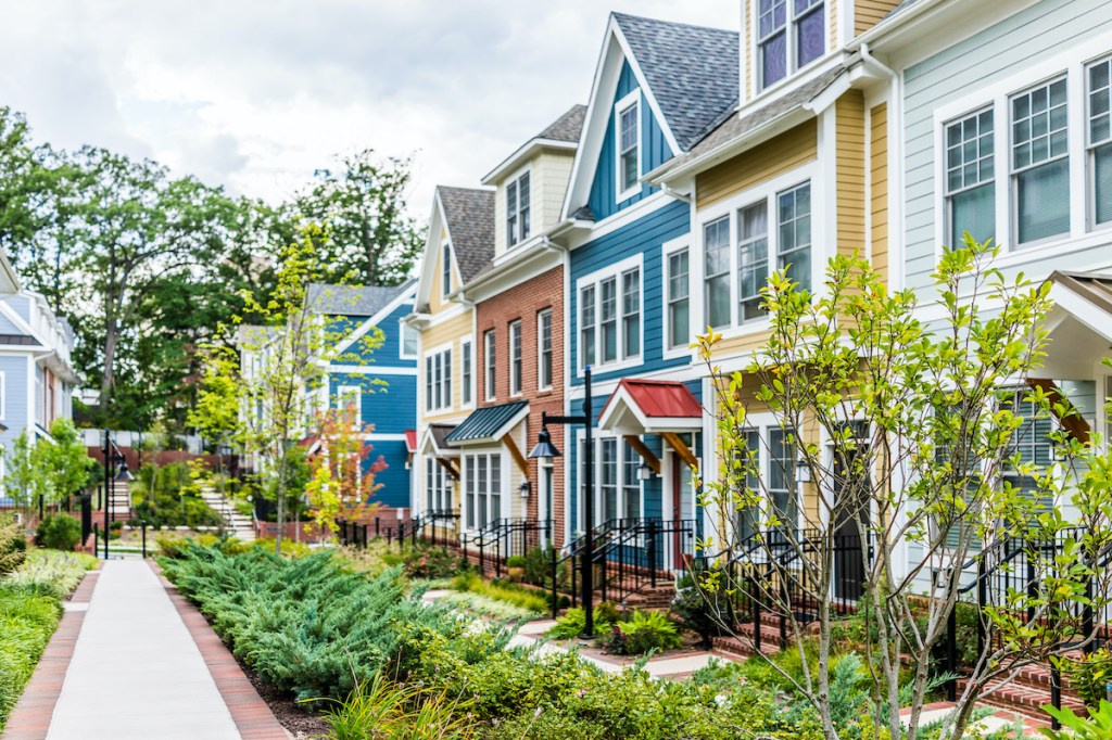 Row of colorful, red, yellow, blue, white, green painted residential townhouses, homes, houses with brick patio gardens in summer