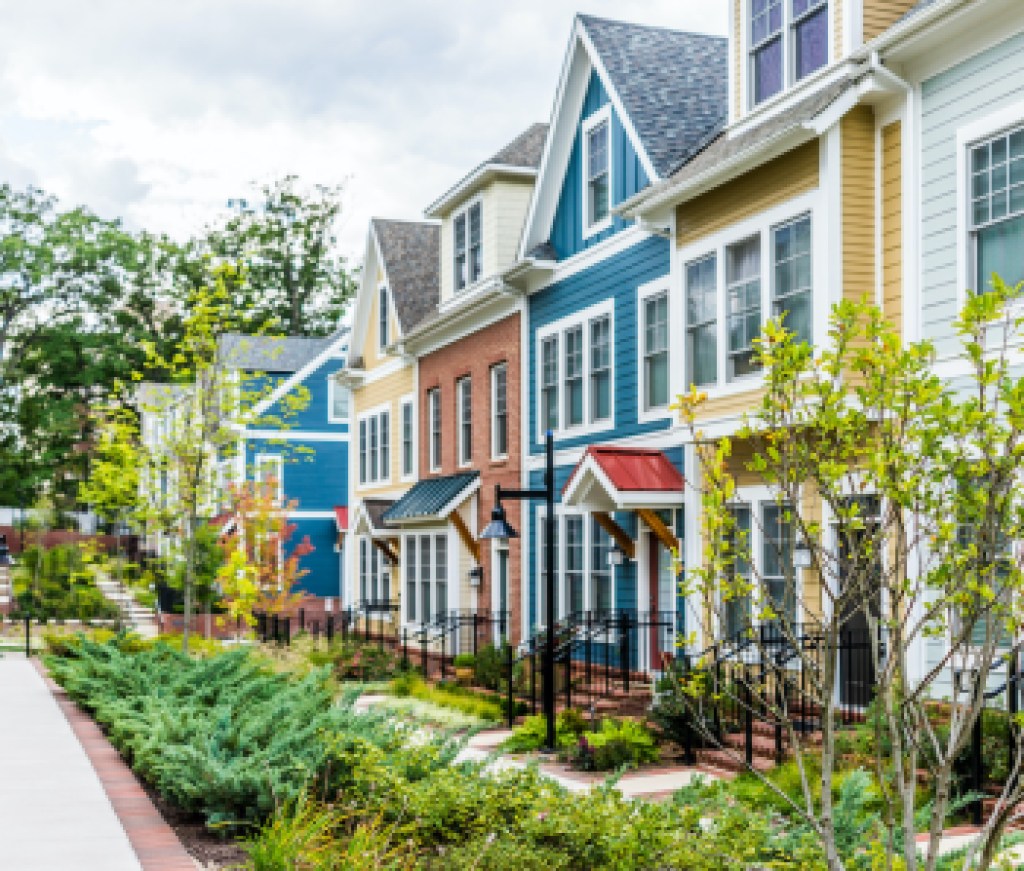 Row of colorful, red, yellow, blue, white, green painted residential townhouses, homes, houses with brick patio gardens in summer