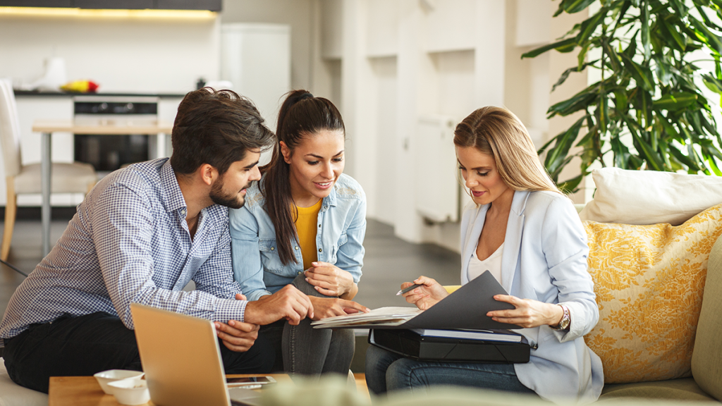 Woman agent with a male and female client; seated in an office lounge overlooking paperwork